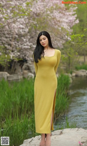 A woman in a yellow dress standing in front of a flowering tree.