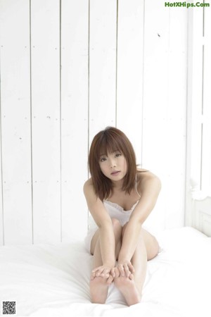 A woman in a white shirt sitting on a bed.