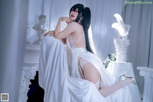 A woman in a white dress sitting on a bed.