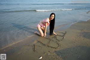 A woman in a pink bikini and a straw hat on the beach.