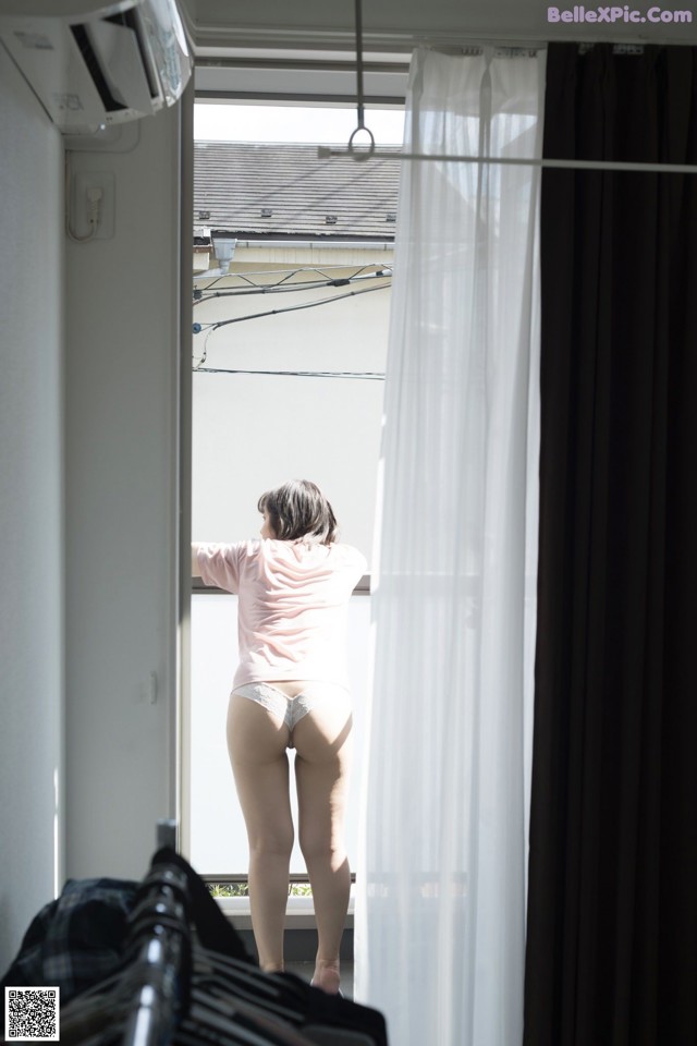 A woman standing in front of a window looking out the window.