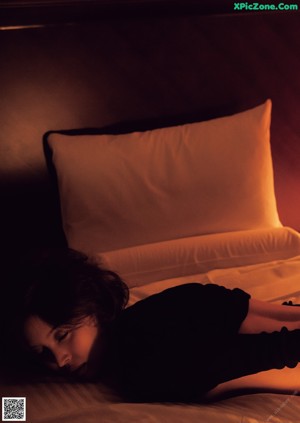 A woman in a black shirt is posing naked on a bed.