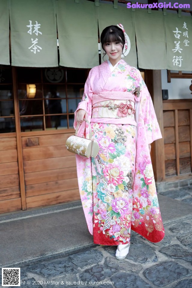 A woman in a pink kimono standing in front of a building.