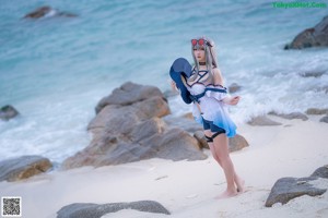 A woman in a bikini holding a stuffed shark on the beach.