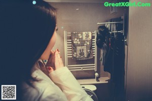 A woman in a white raincoat standing in a bathroom.