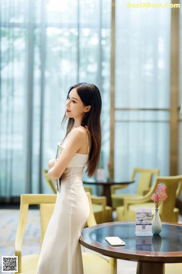 A woman in a white dress standing next to a table.