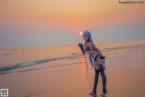 A woman in a bikini standing on a beach at sunset.