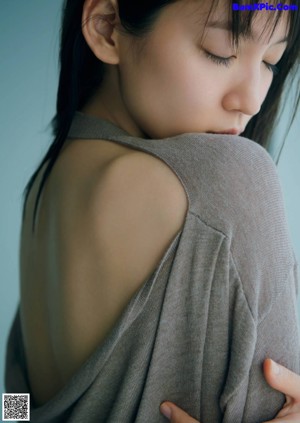 A woman sitting on a window sill wearing a blue sweater.