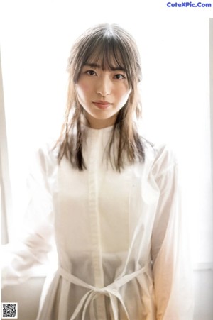 A woman standing in front of a window wearing a white shirt.