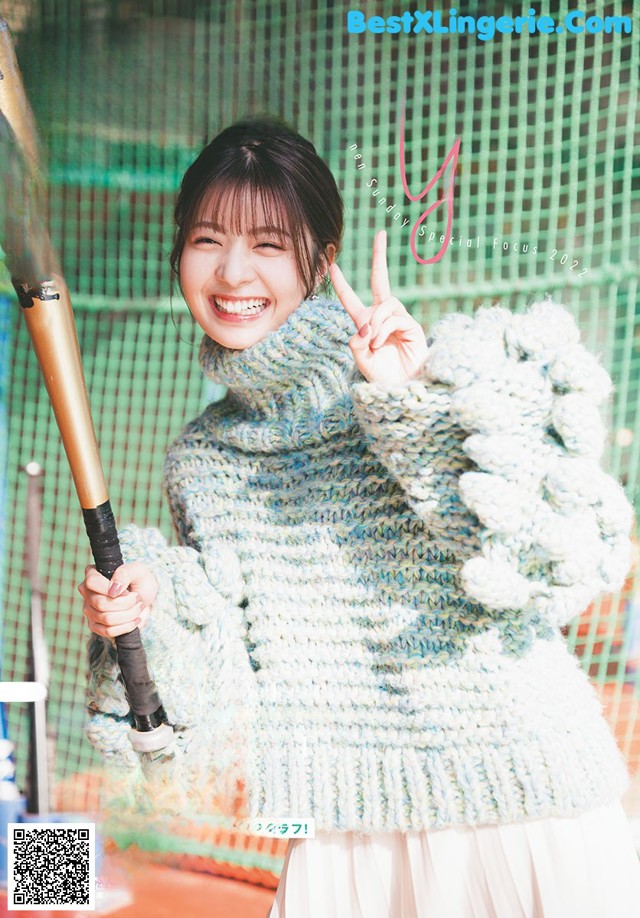 A woman holding a baseball bat in front of a net.