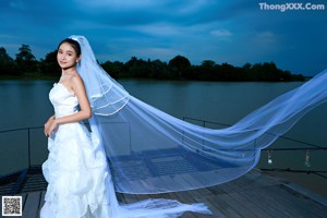 A woman in a wedding dress sitting on a dock.