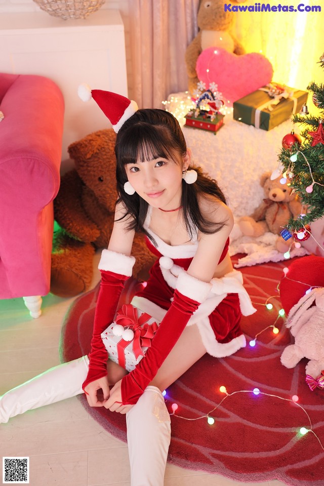 A woman in a santa outfit sitting on the floor next to a Christmas tree.